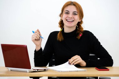 Mutlu genç ofis çalışanı masa başında dizüstü bilgisayarı, cep telefonu ve not defteriyle oturuyor..