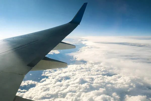 View from airplane on the aircraft white wing flying over cloudy landscape in sunny morning. Air travel and transportation concept.