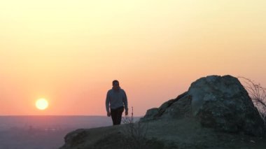 Gün batımında dağlarda tek başına büyük taşlara tırmanan bir yürüyüşçünün silueti. Erkek turist, akşam vakti elini yüksek kayalara kaldırıyor. Turizm, seyahat ve sağlıklı yaşam tarzı konsepti.