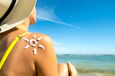 Omzunda güneş kremi ile plajda bronzlaşan genç bir kadının arka görüntüsü. UV güneş yanığı koruması ve güneş kremi konsepti