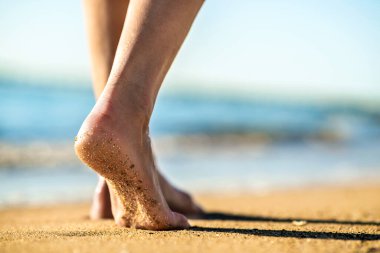 Kadın ayaklarının kumda çıplak ayakla yürürken altın plajda ayak izleri bırakması. Tatil, seyahat ve özgürlük kavramı. Yazın dinlenen insanlar.