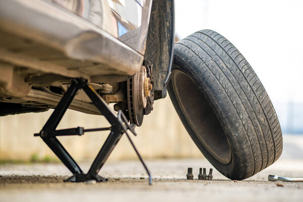 Closeup of a car lifted on jack in process of new wheel tire replacement. Breakdown of a vehicle on a street.