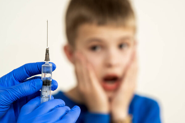 Doctor preparing vaccination injection with a syringe to an afraid child boy. Vaccination of children at school concept.