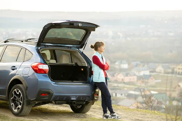 Young woman driver standing alone near her car enjoying view of nature landscape.