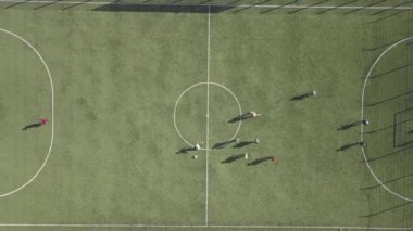 Yeşil futbol sahasının havadan görünüşü ve futbol oynayan oyuncular. Spor faaliyetleri sırasında çimenlerin üzerinde tanınmayan küçük sporcular stadyumu kapladı..
