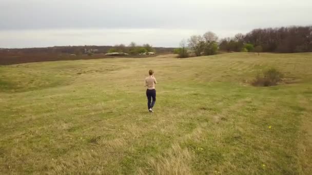 若い女性の空中ビュー単独で空の芝生の上を歩くフィールドをカバー — ストック動画