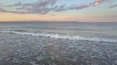 Gün batımında gökyüzünün altında mavi su dalgaları olan bir deniz yüzeyinin havadan görünüşü.