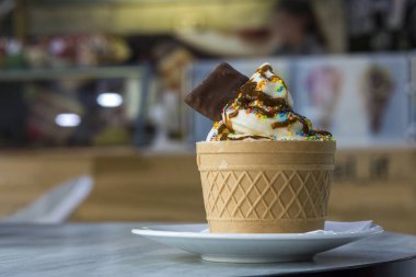 Dondurma Tatlı gofret fincan çikolatalı kurabiye ve yaratıcı dekorasyon Tepesi bulanık renkli iç arka plan üzerinde beyaz plaka.