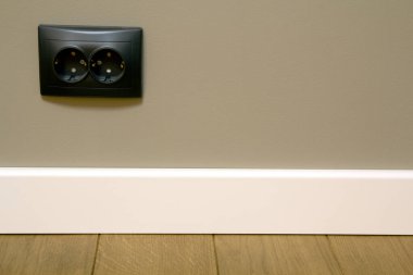 Koyu ahşap meşe parke ve gri duvara monte edilmiş siyah elektrik prizlerini kapatın..