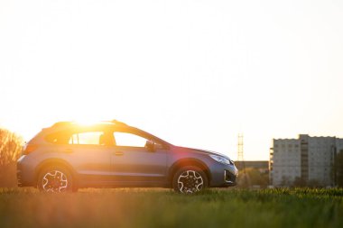 Gün batımında yeşil çimlerin üzerinde mavi arazi arabası. Otomobille seyahat, vahşi yaşam macerası, keşif gezisi ya da bir SUV otomobili ile aşırı seyahat. Offroad 4x4 aracı gün doğumunda arazide olacak..