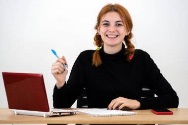 Mutlu genç ofis çalışanı masa başında dizüstü bilgisayarı, cep telefonu ve not defteriyle oturuyor..