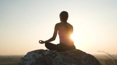 Genç, rahat bir kadın büyük bir taşın üzerinde oturmuş sıcak bir yaz gününün tadını çıkarıyor. Gün batımında meditasyon yapan ve dinlenen bir kız..