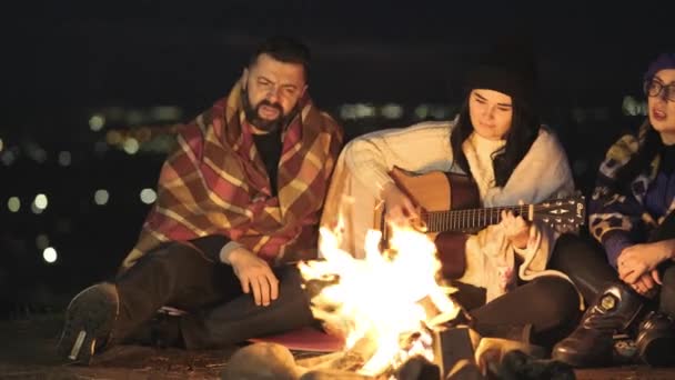 사람들 밖에서 모닥불 근처에 기타를 노래를 부르고 행복하게 이야기하는 즐긴다 — 비디오