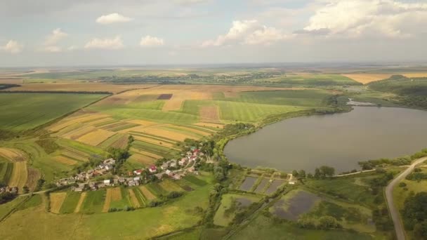 秋の農村部の黄色の農地や小さな村の家に囲まれた湖の空中ビュー — ストック動画