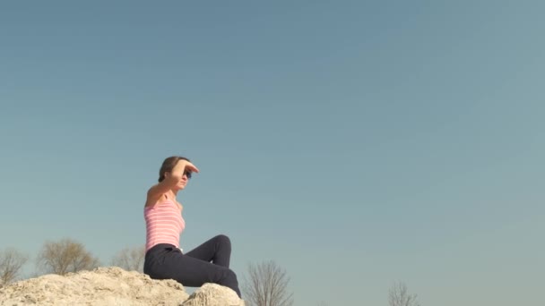 年轻而轻松的女人坐在外面的一块大石头上 享受着温暖的夏日 日落时分 女孩在大自然中沉思和放松 — 图库视频影像