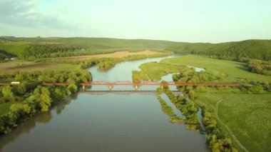 Yeşil kırsal bölgedeki çamurlu geniş nehir üzerindeki dar bir köprünün havadan görüntüsü..