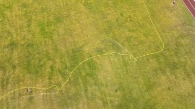 Yeşil çimenler ve su püskürten fıskiyelerle kaplı futbol sahası yüzeyinin yukarıdan görünüşü.
