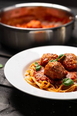 Köfteli spagetti portresi. İtalyan makarna tabağı siyah ahşap arka planda beyaz tabakta servis edilir. Spagetti ve köfte, domates sosunda pişmiş köfteli bolonez sosu gibidir..