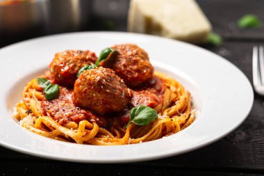 Spagetti ve köfte tabağını yakından çek. İtalyan makarna tabağı siyah ahşap arka planda beyaz tabakta servis edilir. Spagetti ve köfte, domates sosunda pişmiş köfteli bolonez sosu gibidir..