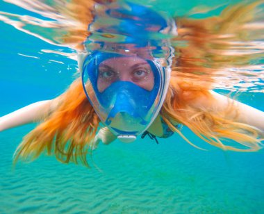 Parlak kırmızı saçlı bir şnorkel kadın. Tam yüz maskesi içinde şnorkel.