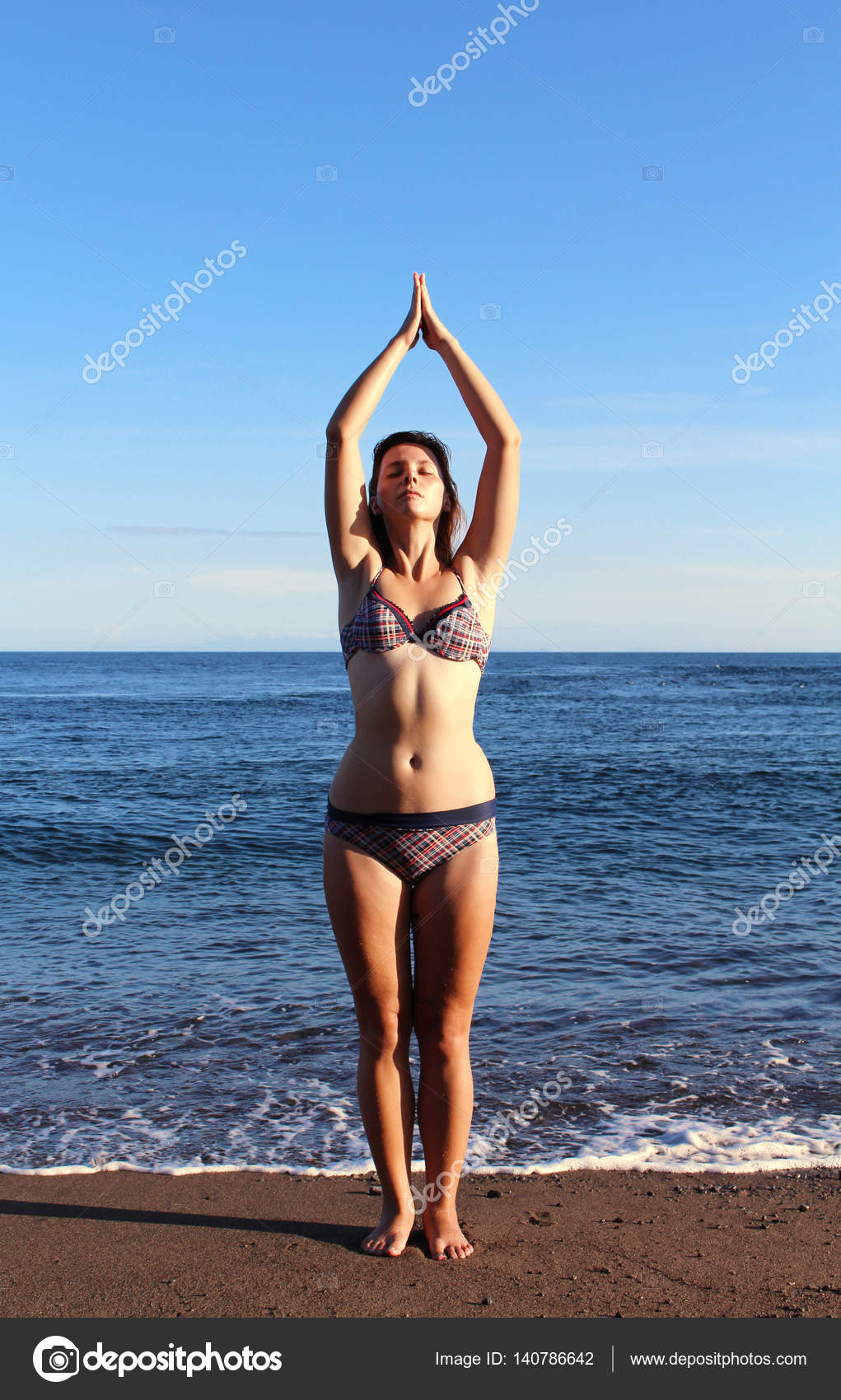 Beautiful woman in swimsuit makes yoga on beach near blue sea — Stock