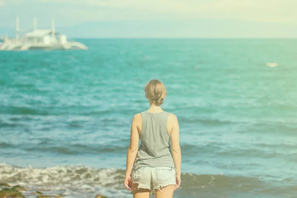 Женщина в рубашке и шортах на пляже. Тонированное фото молодой девушки, смотрящей круизный катер . — стоковое фото