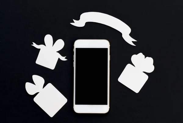 Téléphone blanc avec boîtes-cadeaux et bannière ruban vierge sur fond noir . — Photo