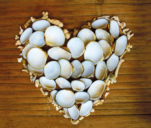 Heart from white corals and shells on wooden background. Marine romance