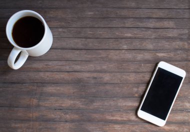 Sıcak rustik ahşap masa üstünde beyaz kahve kupa ve beyaz smartphone