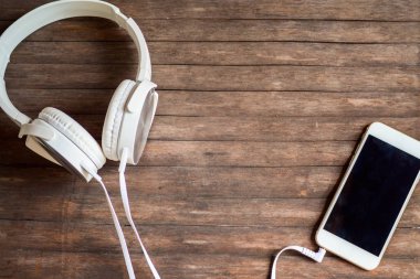 Dokunmatik ekran telefon masada. Beyaz kulaklık ve ahşap arka plan üstünde smartphone.