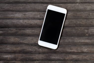 Koyu ahşap masa üstünde beyaz smartphone. Eski püskü şık arka plan üzerinde siyah ekran smartphone.