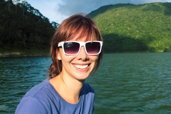 Female face with smile on the background of forest lake. Girl on lake or river boat trip.