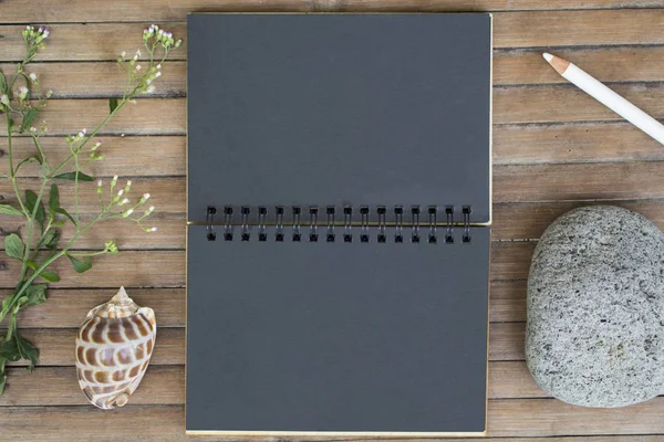 Black paper notebook on rustic wooden background with natural decor.