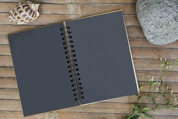 Black paper notebook on rustic wooden background with natural decor.