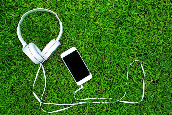 Auriculares y teléfono en hierba verde. Escuchar música concepto foto . —  Fotos de Stock
