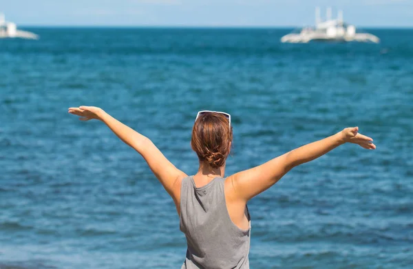 Женщина с поднятыми руками на фоне моря. Счастливая девушка в непринужденной одежде . — стоковое фото