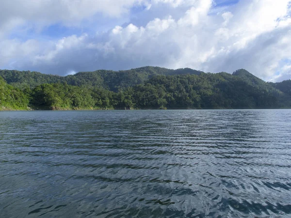 Small waves on lake water. Green hills and cloudy sky. Natural volcanic lake