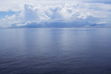 Hala mavi su ve tropikal ada ile sahil manzara. Uzak ada ile deniz manzarası. Okyanusun üstündeki beyaz kabarık bulutlar. Deniz ve gökyüzü minimal fotoğraf arka plan. Yaz seyahatinde rahatlatıcı Panorama