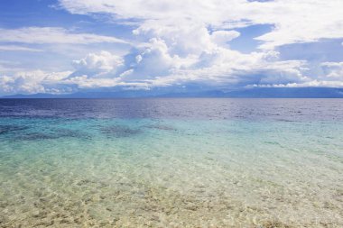 Turkuaz su ve tropikal ada ile deniz manzara. Uzak ada deniz manzaralı. Beyaz kabarık bulutların üzerinde mavi okyanus. Deniz ve gökyüzü çok az fotoğraf arka plan. Beyaz kum ile pastoral sahil