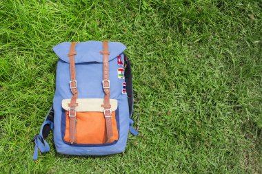 Hipster backpack on summer green grass. Summer travel background photo. Sunny grass lawn with blue backpack. Hipster outdoor banner template with text place. Nomadic lifestyle. Holiday in countryside clipart