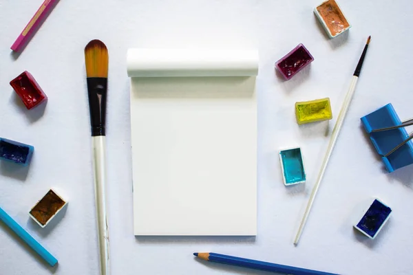 Herramientas de arte y bloc de notas en blanco sobre mesa blanca. Suministro de arte de pintura - pincel, acuarela, lápiz . — Foto de Stock