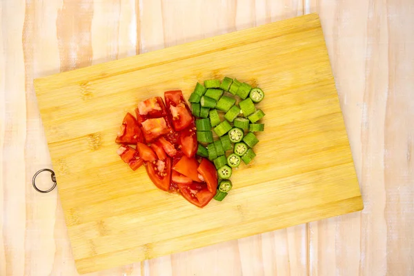 Tomato and okra vegetables cut on cutting board. Healthy vegetarian salad preparation. Green and red vegetable