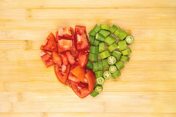 Tomato and okra vegetables in heart shape on cutting board. Vegetables cut top view photo on wooden background