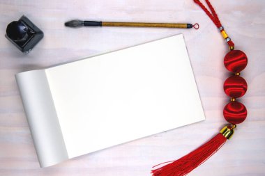 Blank open notebook page and calligraphy supplies. Oriental decoration flat lay on white wooden table.