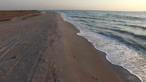 Voando para trás sobre a praia de areia ao longo da linha de surf durante o pôr do sol — Vídeo de Stock