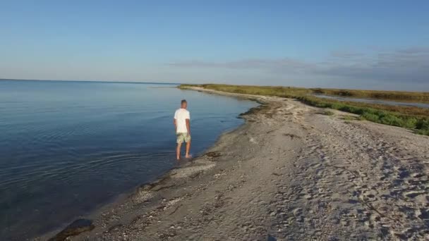 Człowiek jest chodzenie wzdłuż dzikiej plaży podczas sunrise — Wideo stockowe
