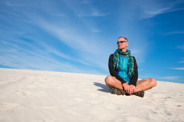 Uśmiechnięty mężczyzna wycieczkowicz siedzi i w pustyni — Zdjęcie stockowe