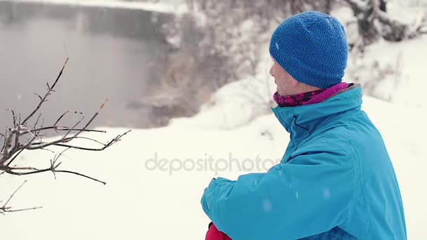 Homme barbu rêveur assis sur la rive du lac pendant les chutes de neige — Video