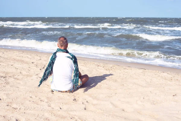 Человек в шарфе сидит на пляже — стоковое фото