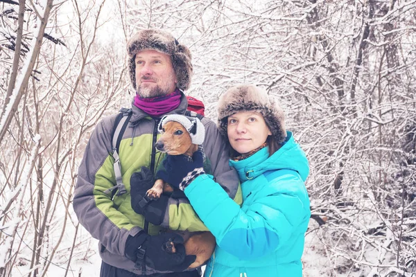 Смолящая пара с маленькой собачкой в забавных зимних люках — стоковое фото